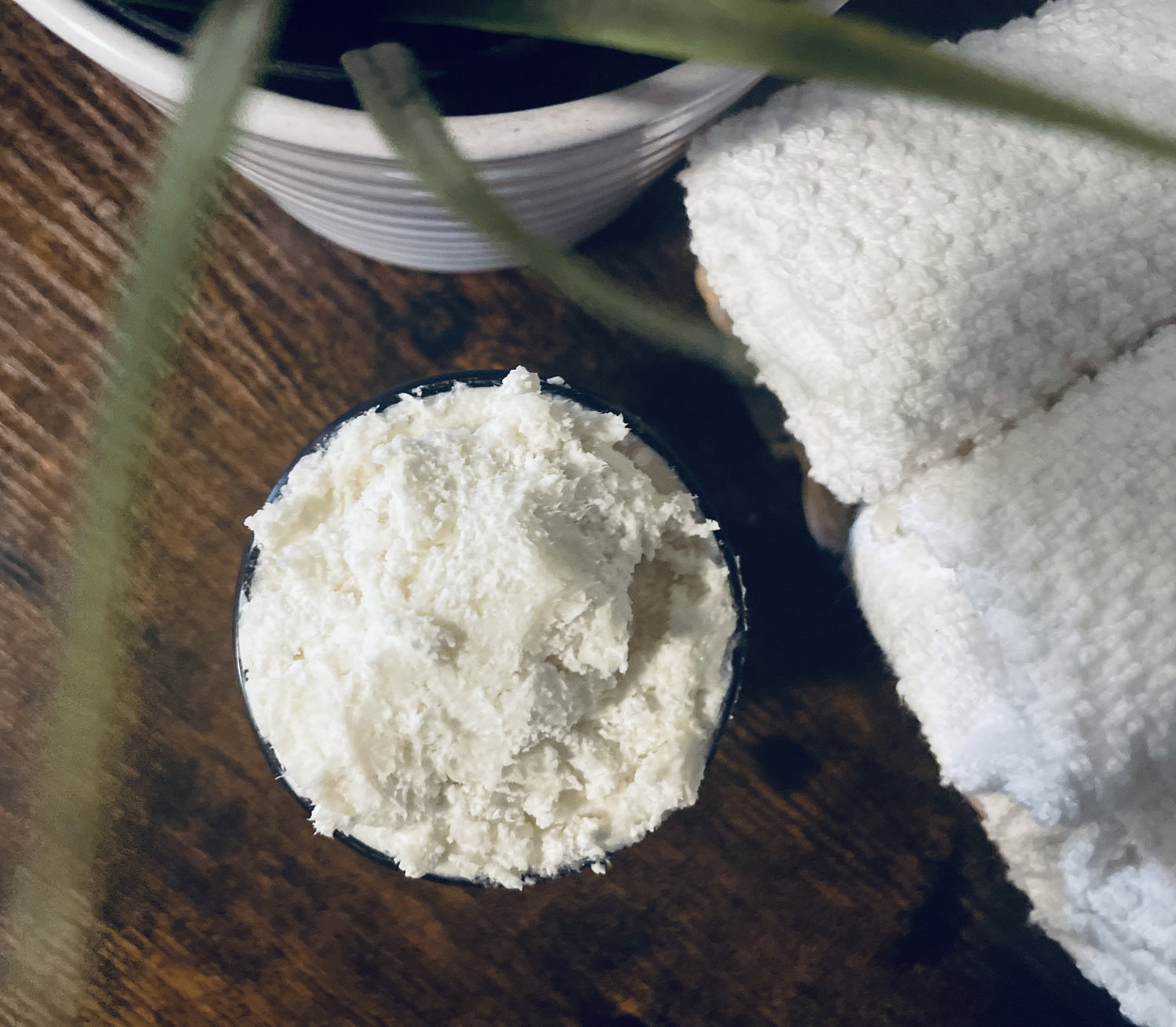 Close up view of body butter texture with white towels and greenery in the background